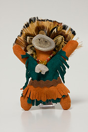 a small doll-like fetish with a headdress of feathers, beaded necklace, mask and dress made of leather.